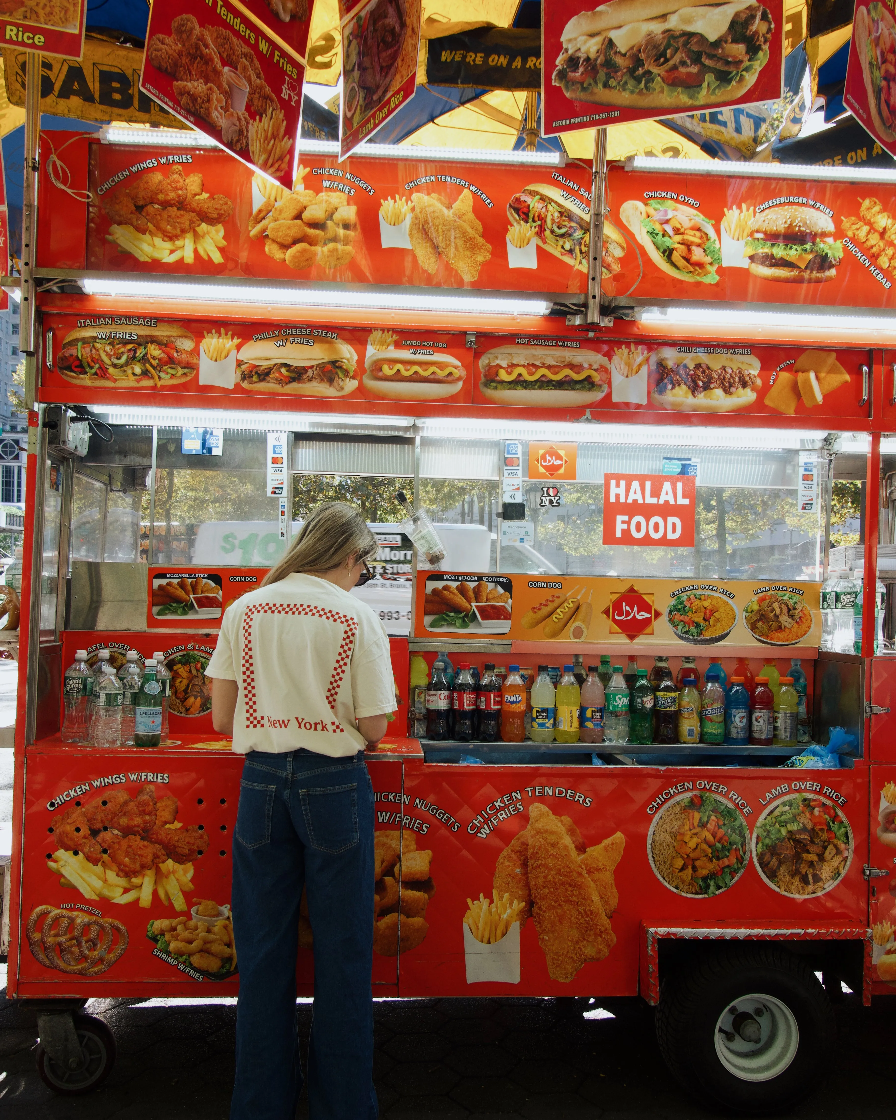A traveler in a Paradise & Main tee ordering at a New York halal food cart