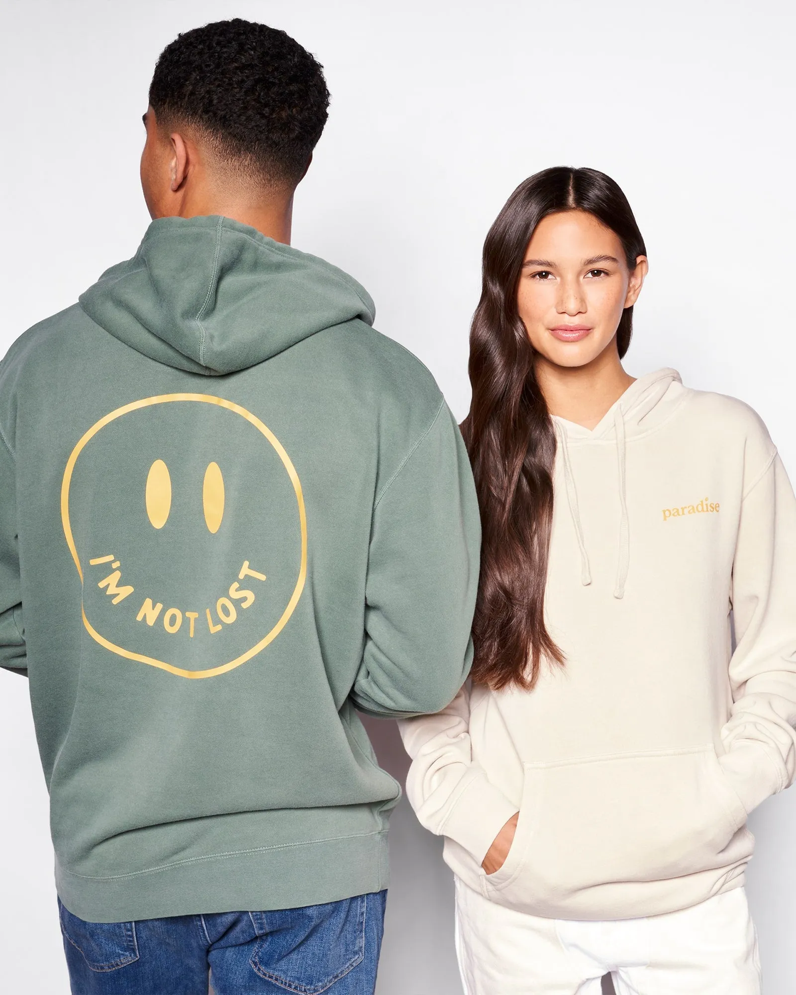 Two friends back to back in I'm Not Lost hoodies, sage green and cream