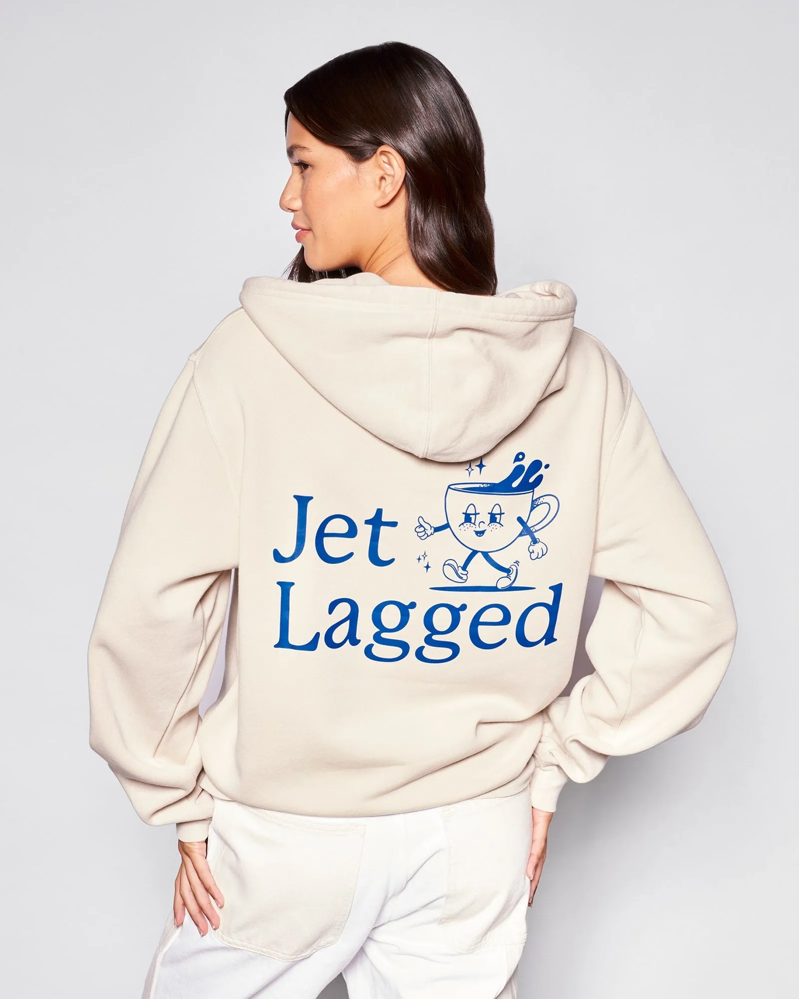 The back of a cream Jet Lagged hoodie, worn on an overcast beach morning