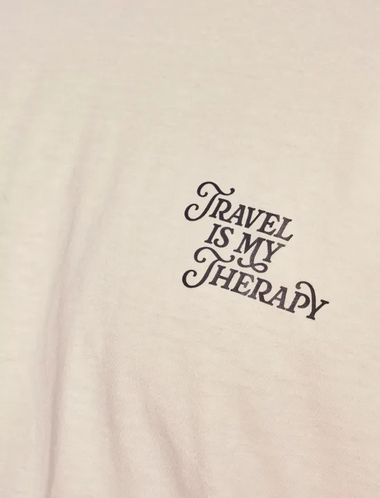 Close-up of the Travel Is My Therapy embroidery on a cream tee